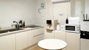 A modern kitchen with white cabinets, a round white table, two wooden stools, a built-in oven, a microwave, and a coffee maker. - Yellow stay (Bucheon)