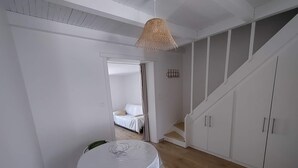 Una habitación con una mesa redonda, una silla verde, una escalera y una cama al fondo.