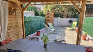 Un patio al aire libre con una mesa, sillas, una pérgola de madera y una parrilla.
