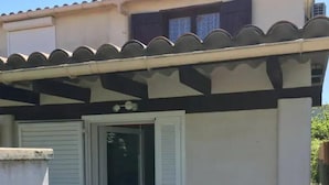 Un edificio con techo de tejas, un porche cubierto y una puerta, y una ventana pequeña.