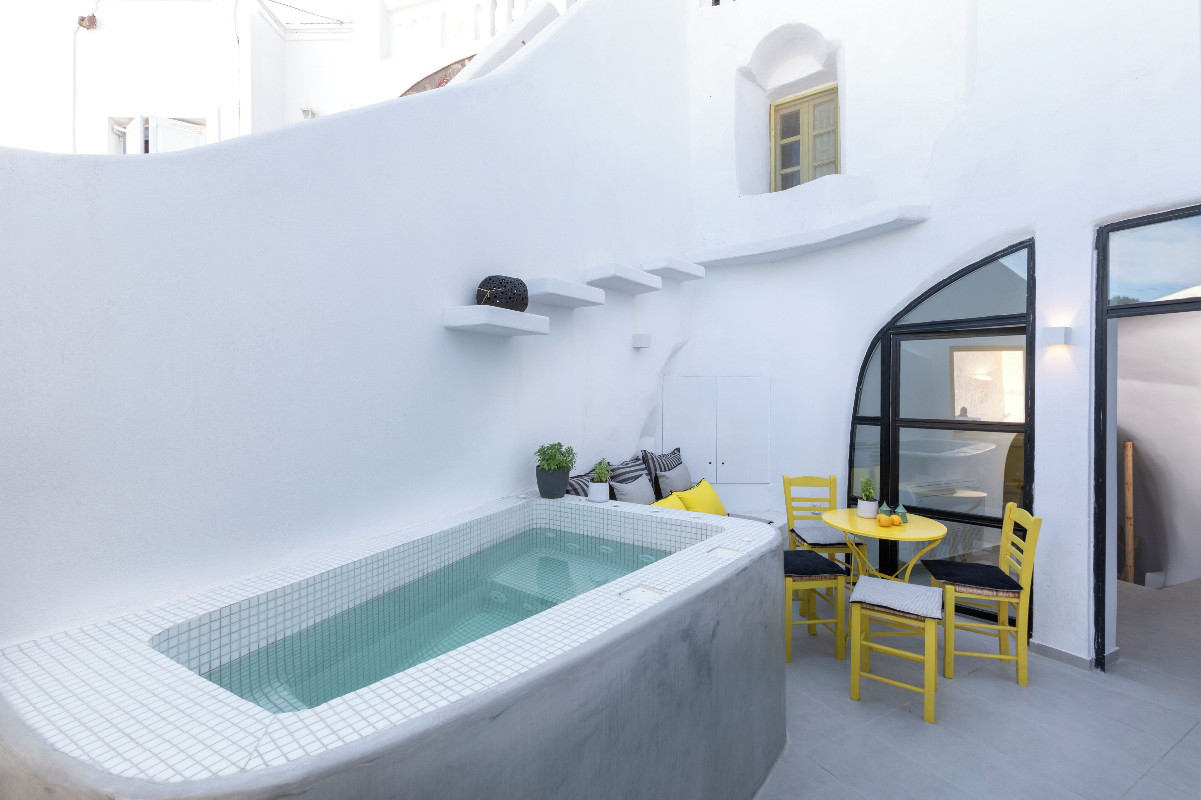 Un espace extérieur moderne doté d’une piscine rectangulaire, de chaises jaunes et d’une petite table.