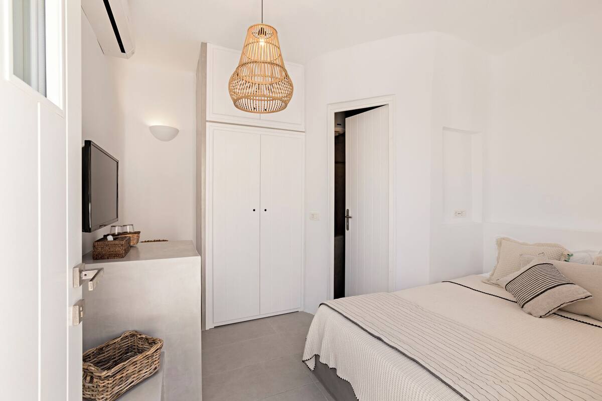 Een slaapkamer met een bed, een televisie, een rieten mand en een deur.