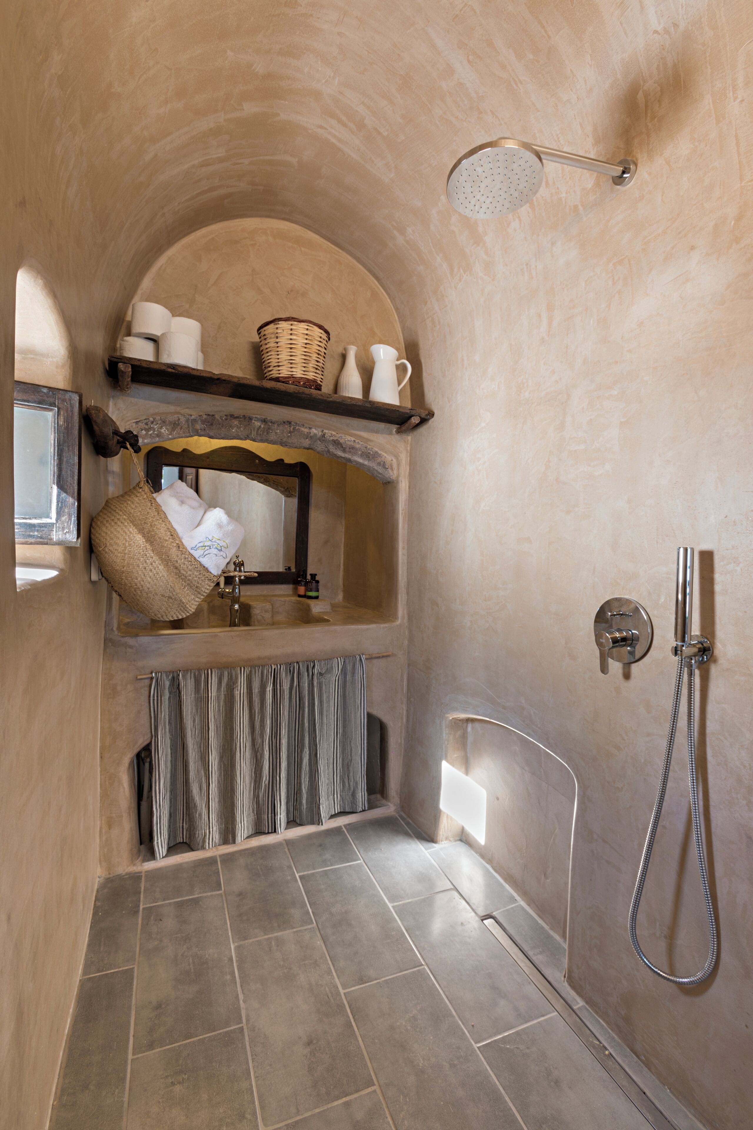 A bathroom with a stone wall, a sink, a shower, and a towel hanging on the wall.
