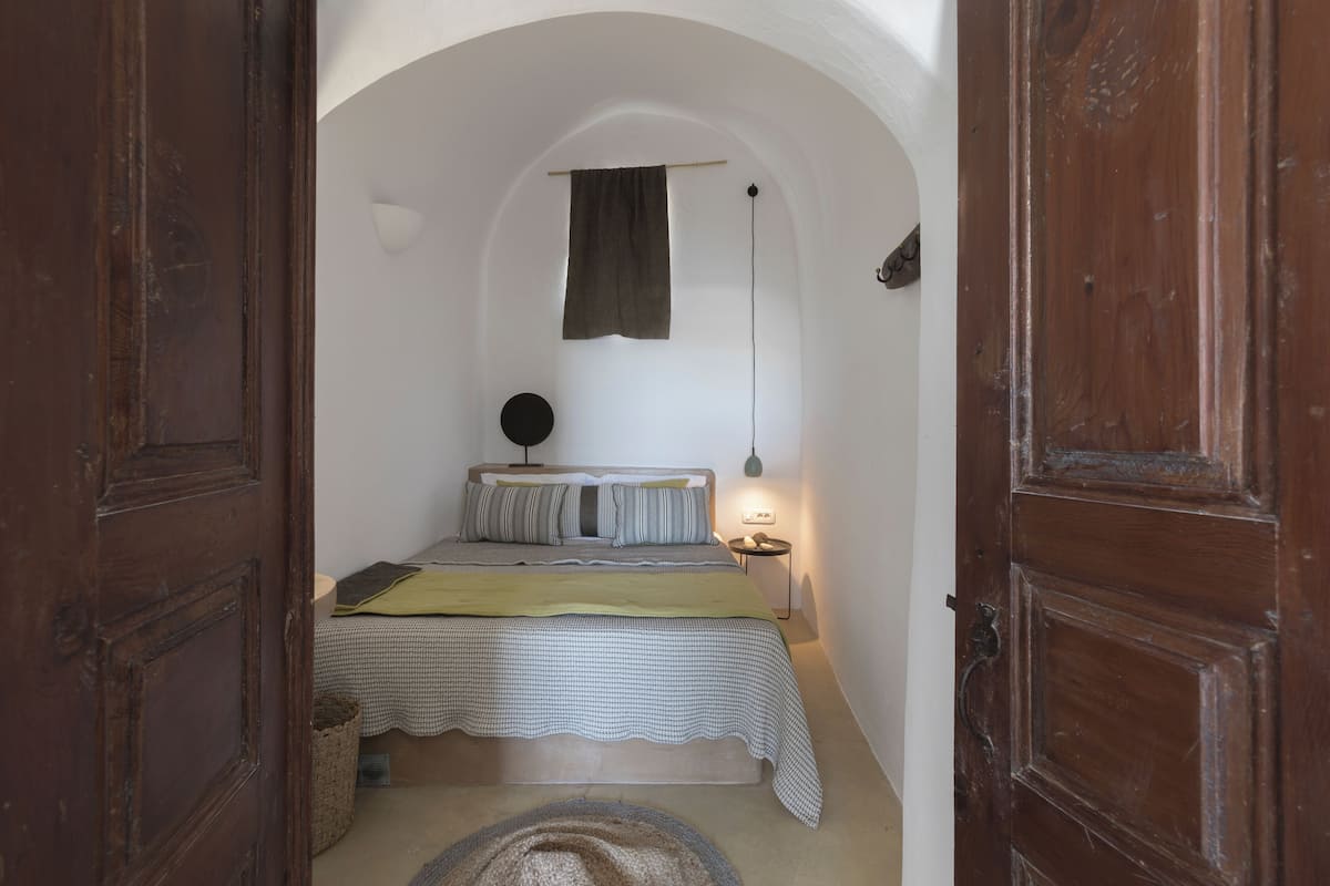 Een smalle gang die leidt naar een slaapkamer met een bed, nachtkastje, lamp en een handdoek.
