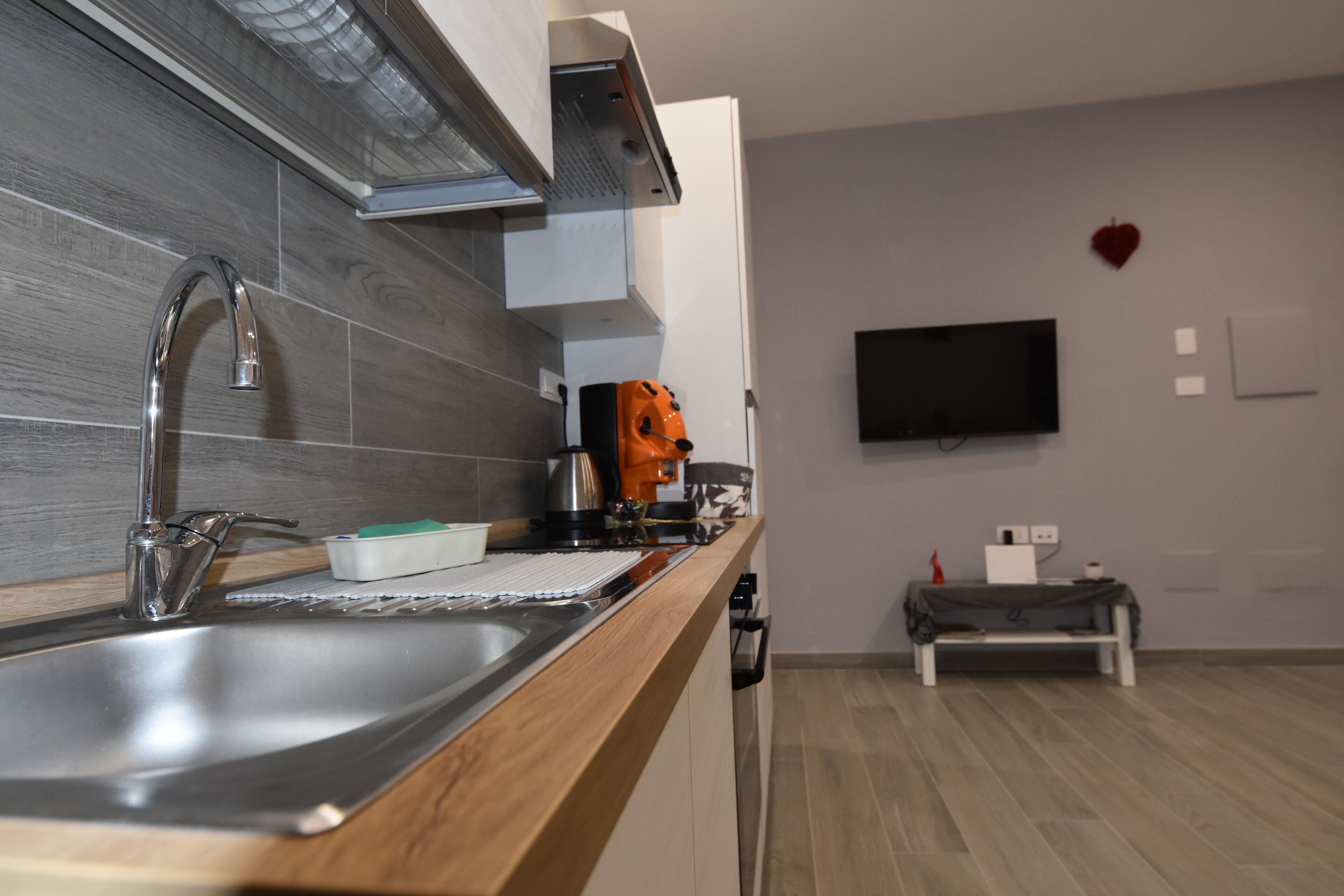 Une cuisine moderne dotée d’un évier en acier inoxydable, d’un plan de travail en bois, d’une machine à café et d’un téléviseur à écran plat fixé au mur.