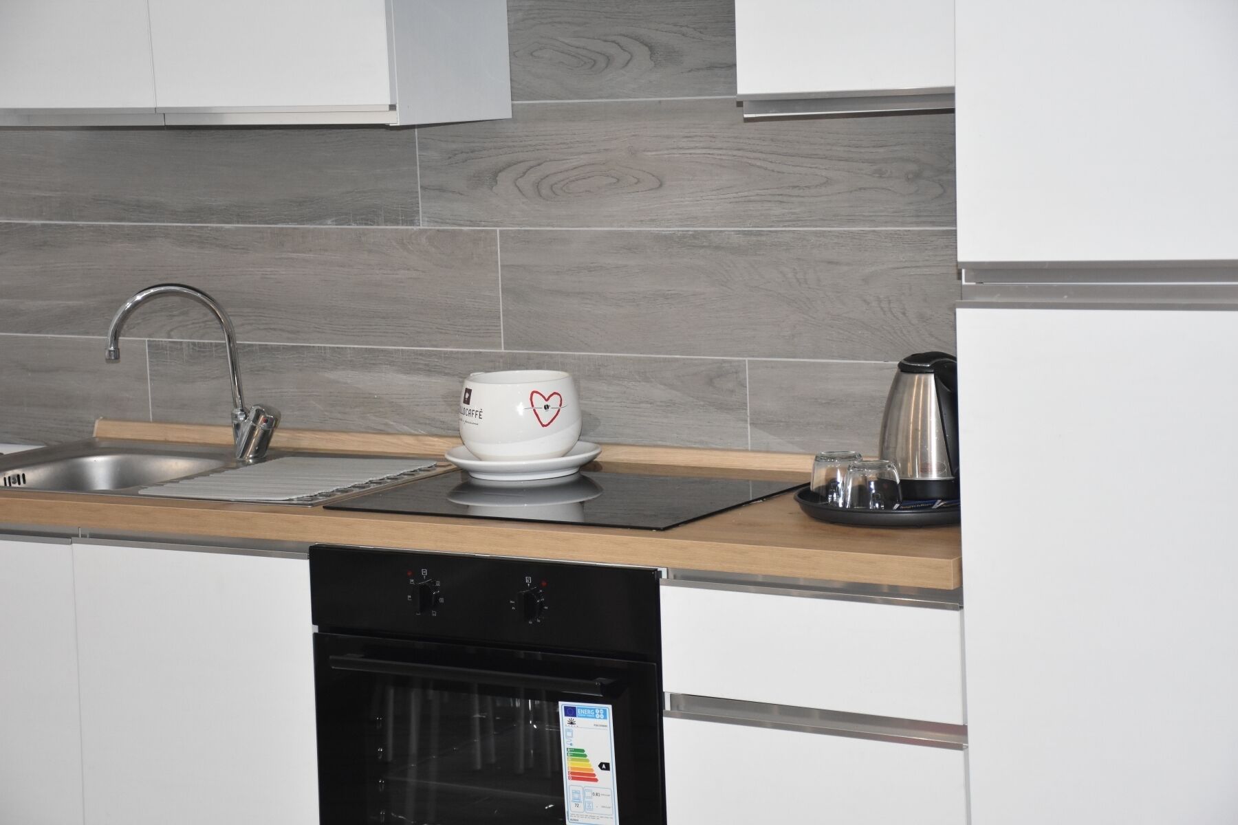 Una cucina moderna con lavello in acciaio inossidabile, una macchina per il caffè e un bollitore sul piano di lavoro.