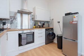 Una cocina moderna con armarios blancos, un refrigerador de acero inoxidable, horno empotrado, lavadora y un cubo de basura.