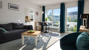 Ein modernes Wohnzimmer mit einer Couch, einem Holztisch und Blick auf einen Balkon mit Tisch und Stühlen.