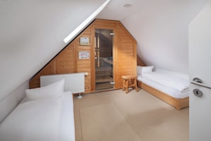 Ein kleiner Raum mit schrägem Dach, Holzvertäfelung, einem weißen Heizkörper, einem kleinen Holzschemel und einem Bett mit weißer Bettwäsche.