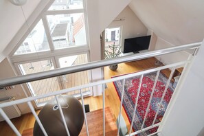 A high-ceilinged room with a large window, a wooden floor, and a red patterned rug. - // Holiday apartment NEY 3 // (Norderney)