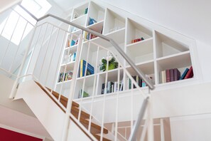 A staircase with white railings and wooden steps leading to a white bookshelf filled with books and a small vase with flowers. - // Holiday apartment NEY 3 // (Norderney)
