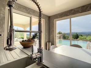 Une cuisine moderne dotée d’une grande fenêtre donnant sur une piscine et des montagnes.
