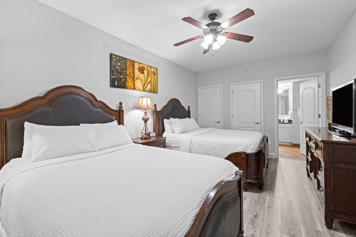 Une chambre d’hôtel avec deux lits, un ventilateur de plafond, un tableau et un téléviseur posé sur une commode.