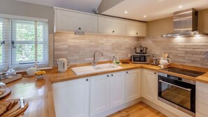 A modern kitchen with white cabinets, a wooden countertop, a stainless steel range hood, and a built-in oven. - The Gate Lodge - One Bed Cottage - Pet Free - Nr Finchingfield & Saffron Walden (Little Bardfield)