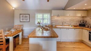 A modern kitchen with a wooden island, white cabinets, and a window with blinds. - The Gate Lodge - One Bed Cottage - Pet Free - Nr Finchingfield & Saffron Walden (Little Bardfield)