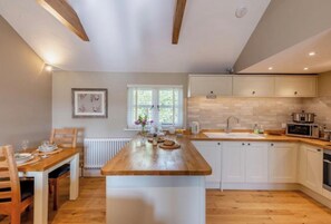 A modern kitchen with a wooden island, white cabinets, and a window with blinds. - The Gate Lodge - One Bed Cottage - Pet Free - Nr Finchingfield & Saffron Walden (Little Bardfield)