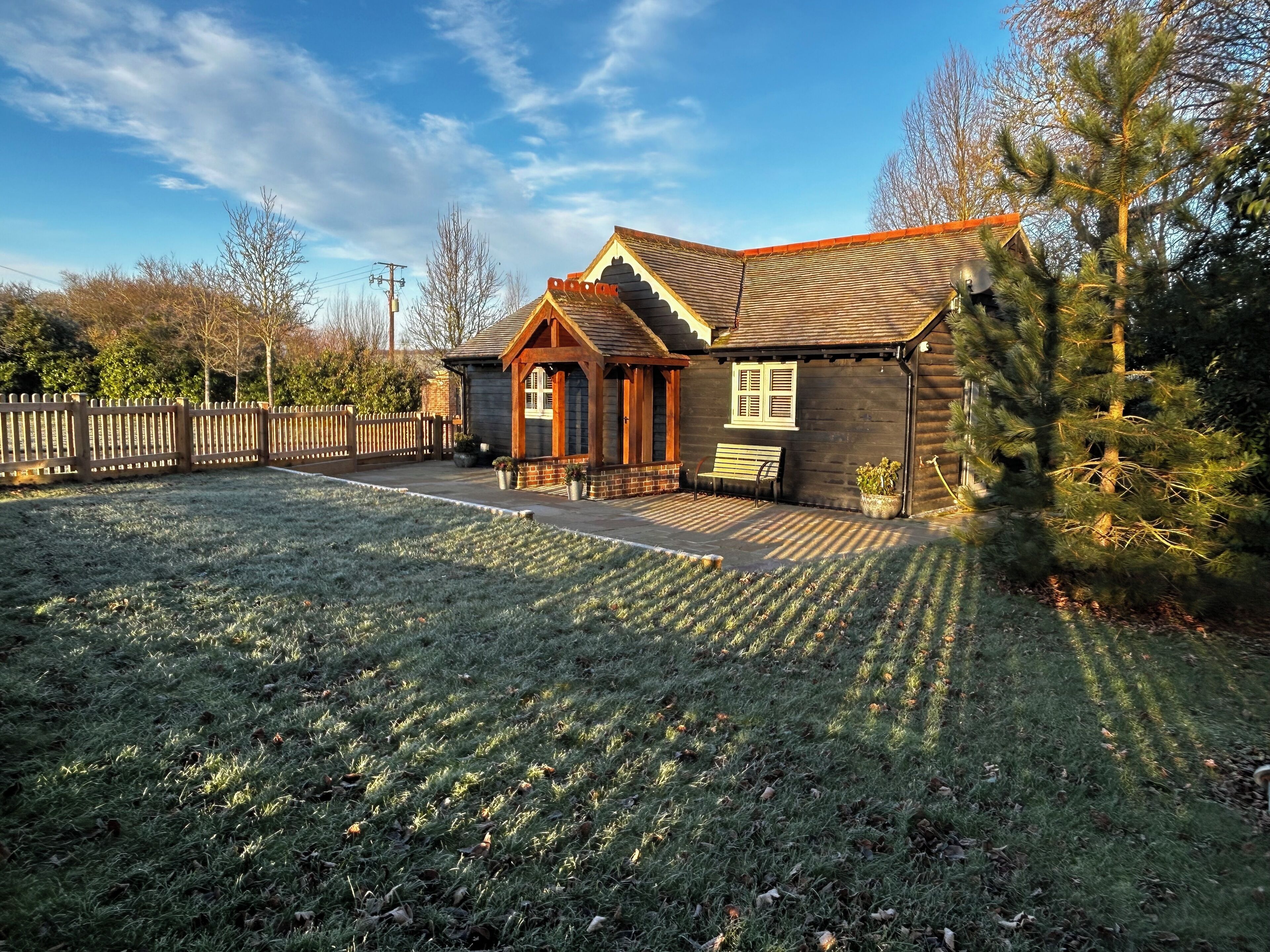 Une cabane en bois avec une véranda, un banc et une cour clôturée.