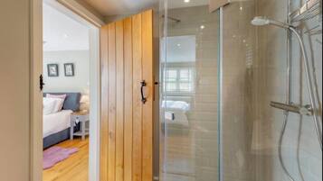 Une salle de bain moderne dotée d’une cabine de douche en verre et d’une porte en bois donnant sur une chambre.