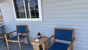Twee houten stoelen met blauwe kussens op een veranda met een kleine tafel, een lantaarn en een raam erboven.