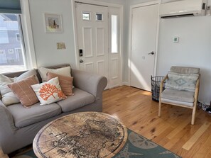 A living room with a grey sofa, a round coffee table with a map, a wooden chair, and a white door. - Experience coastal charm at Sand Dollar, a spacious 4-bedroom retreat in Ferry Beach, Saco, ME. (Saco)