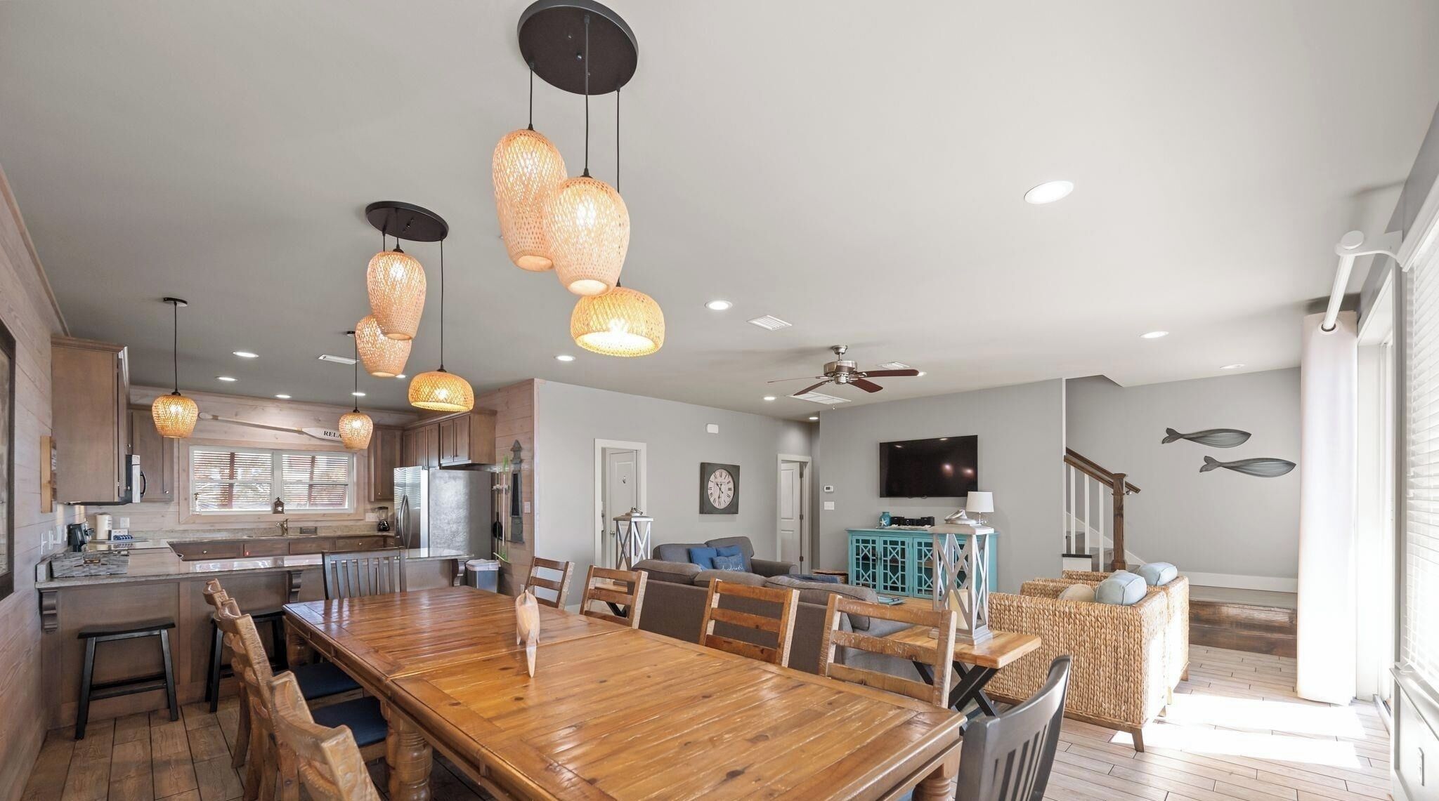 A spacious kitchen with wooden cabinets, a large dining table, and hanging pendant lights.