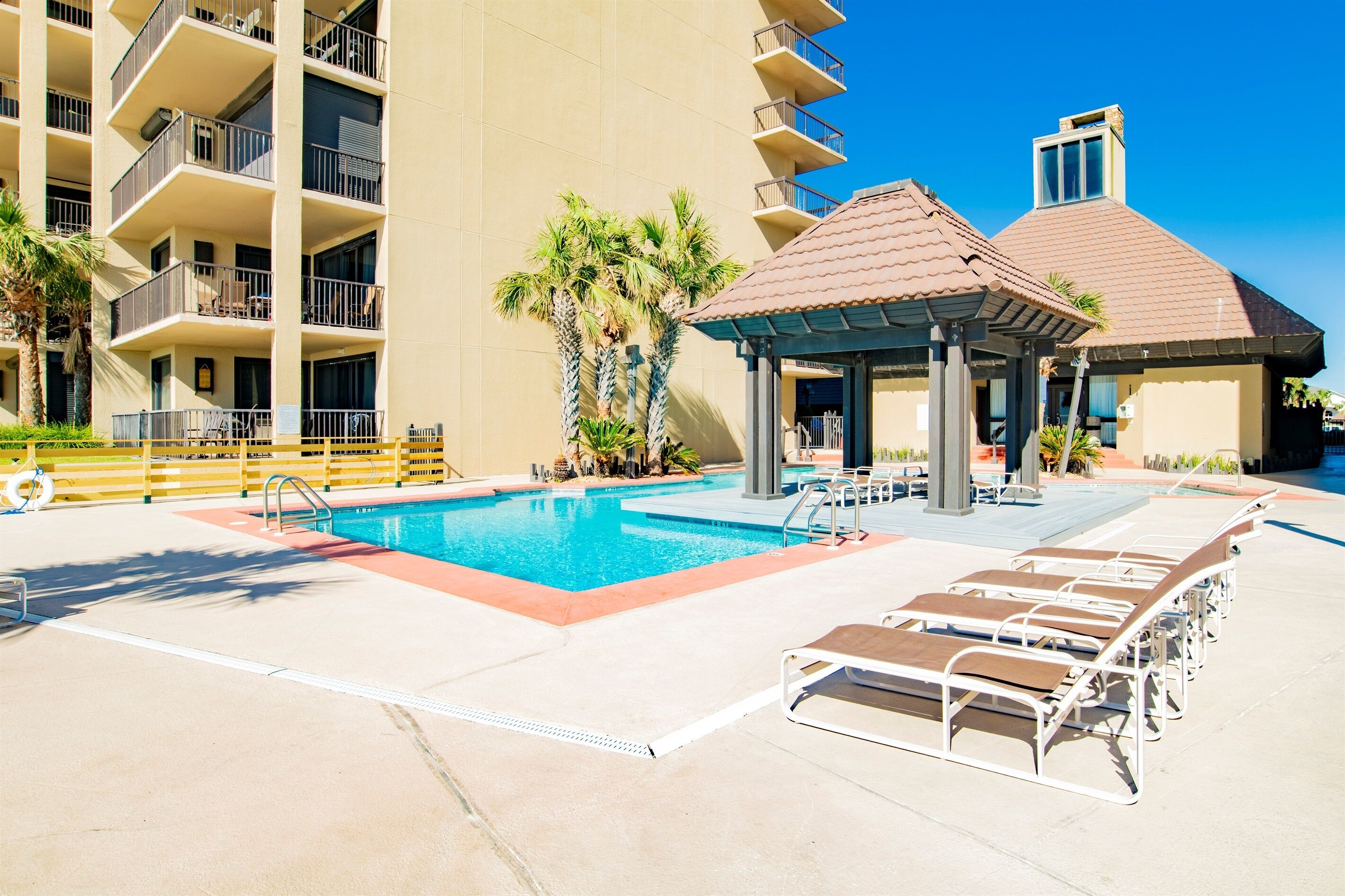 A swimming pool with lounge chairs, a gazebo, and a multi-story building with balconies.