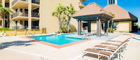 A swimming pool with lounge chairs, a gazebo, and a multi-story building with balconies.