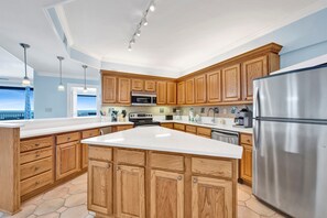 A spacious kitchen with wooden cabinets, a stainless steel refrigerator, and a large island. - Dog Friendly Beachfront Paradise East Corner Unit (Orange Beach)