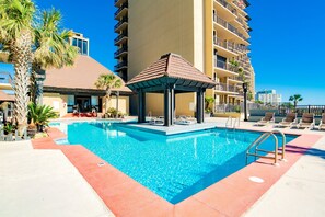 A swimming pool with lounge chairs, a gazebo, and a tall building in the background. - Dog Friendly Beachfront Paradise East Corner Unit (Orange Beach)