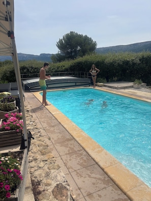 Ein Schwimmbecken mit klarem, blauem Wasser, umgeben von Steinplatten und Blumenbeeten.