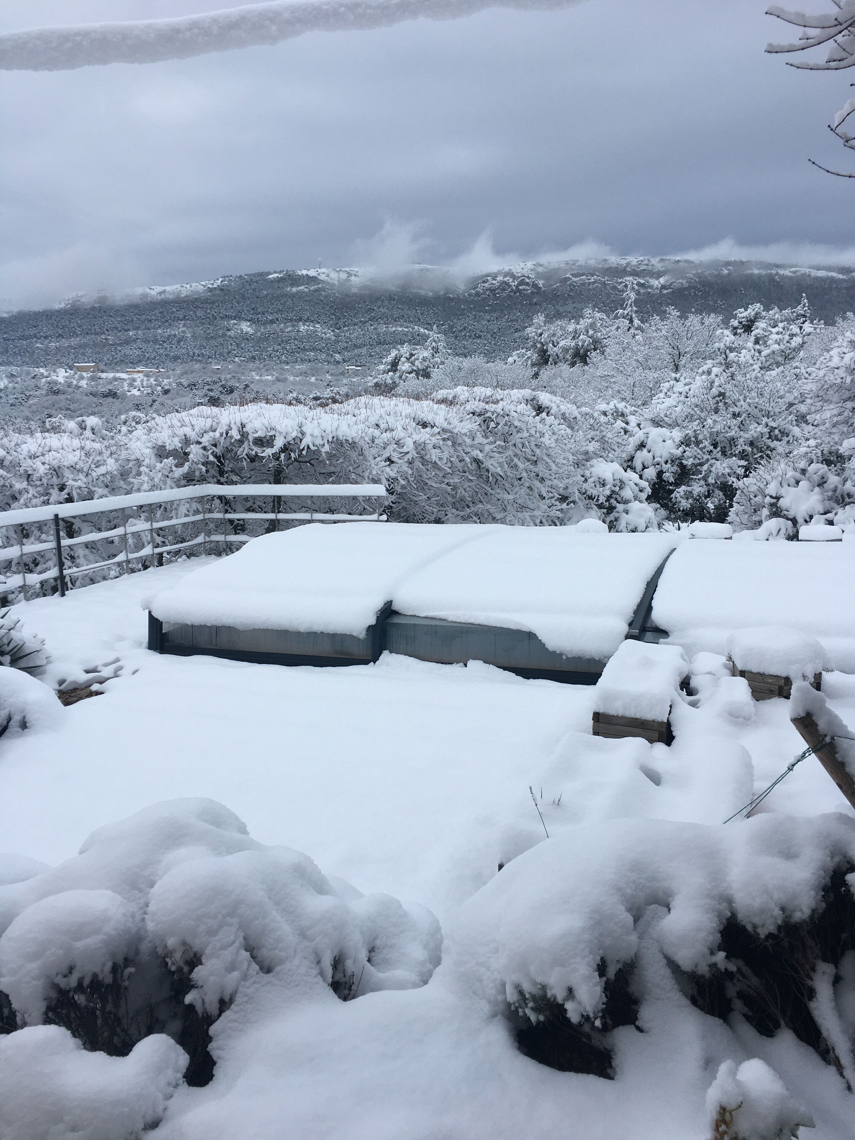 Schneebedecktes Freigelände mit einer Steinmauer und Stufen, die zu einer Holzterrasse führen.