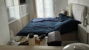 Ein Schlafzimmer mit Bett, Nachttisch, Lampe und einem Fenster mit Vorhängen.