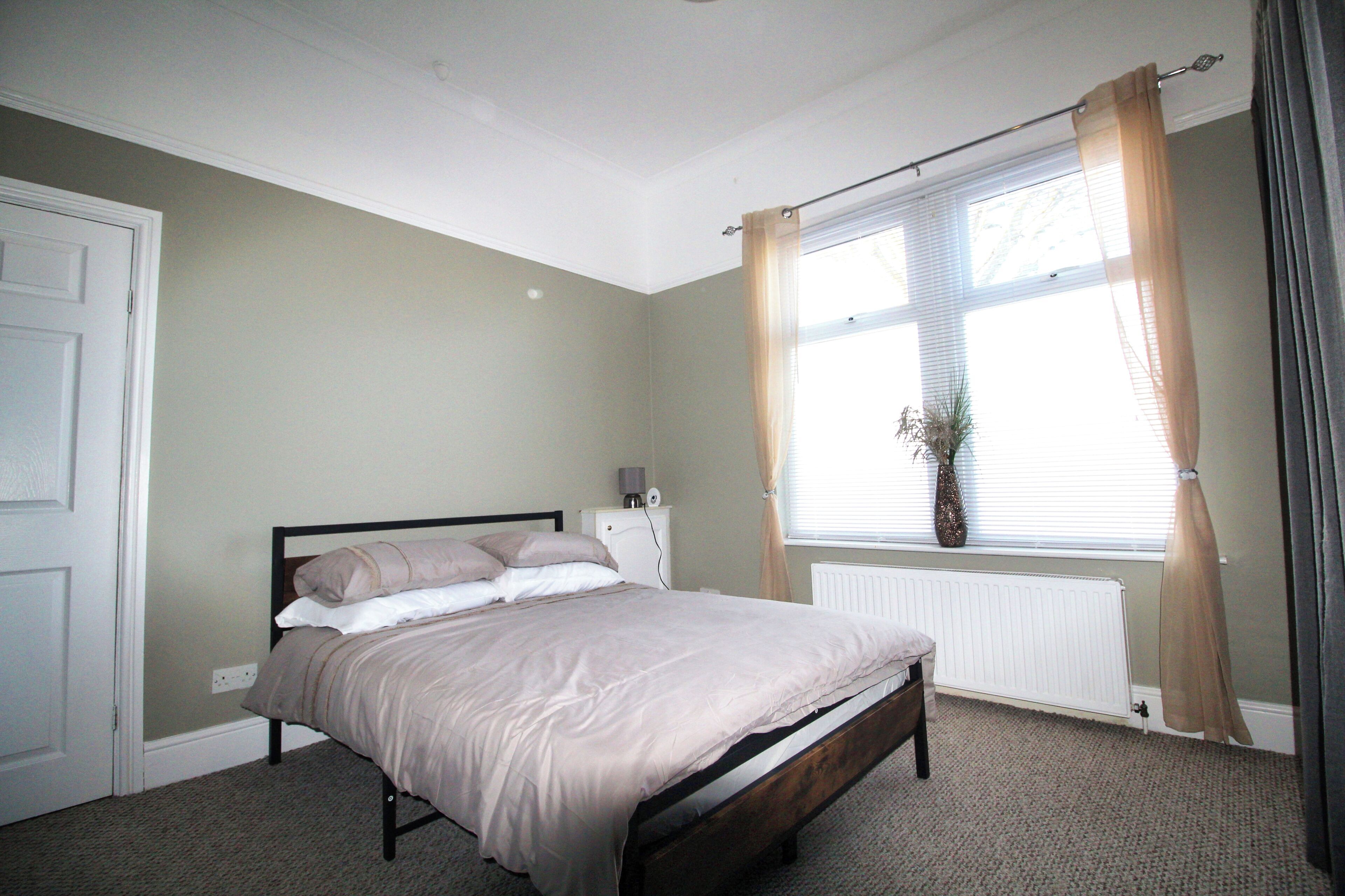 Ein Schlafzimmer mit einem Bett, einem Heizkörper, einem Fenster mit Vorhängen und einer Tür.