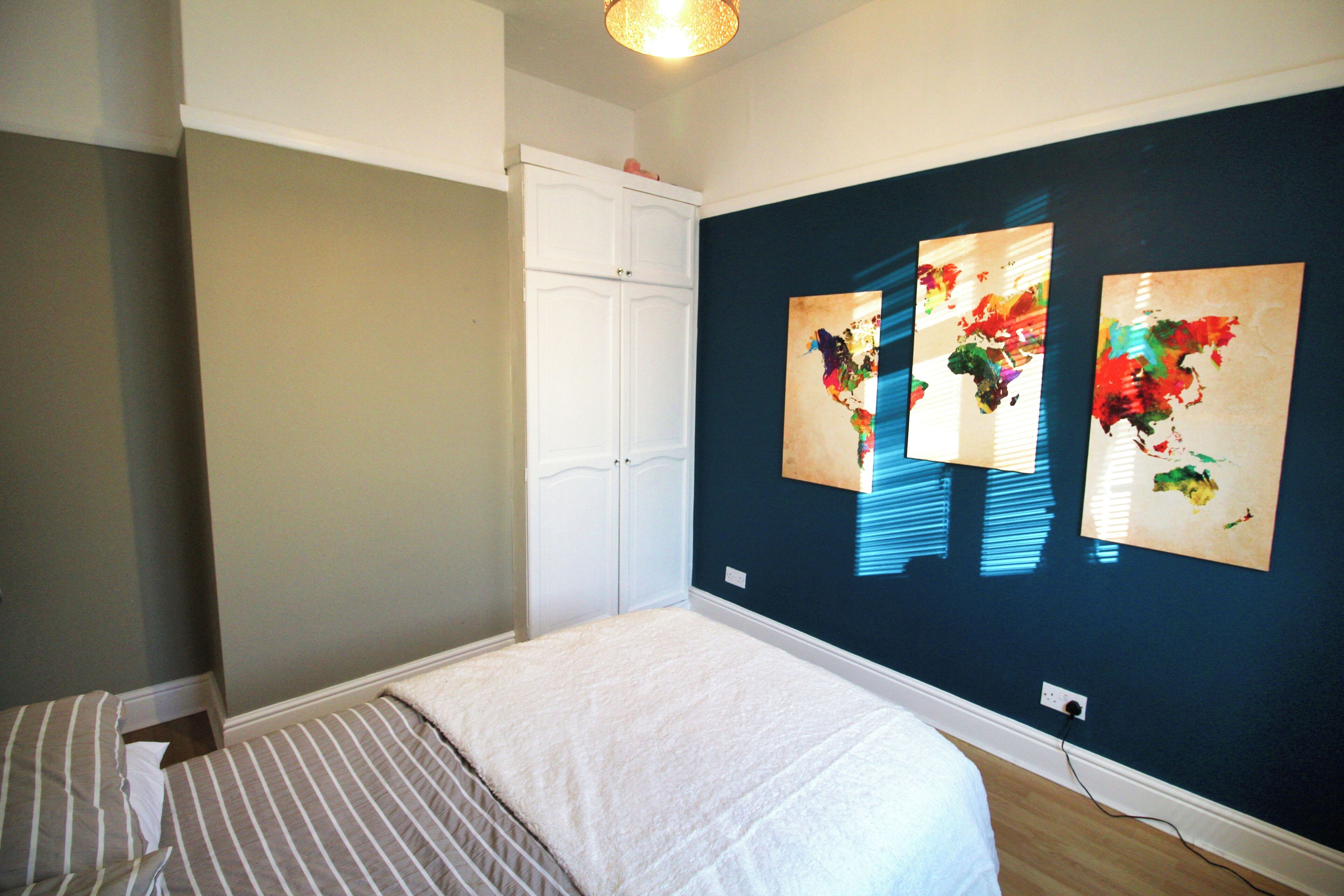 Une chambre à coucher comprenant un lit, une armoire et trois tableaux abstraits accrochés au mur.