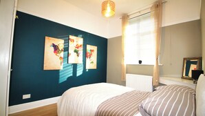 Un dormitorio con cama, ventana con cortinas, radiador y tres obras de arte colgadas en la pared.