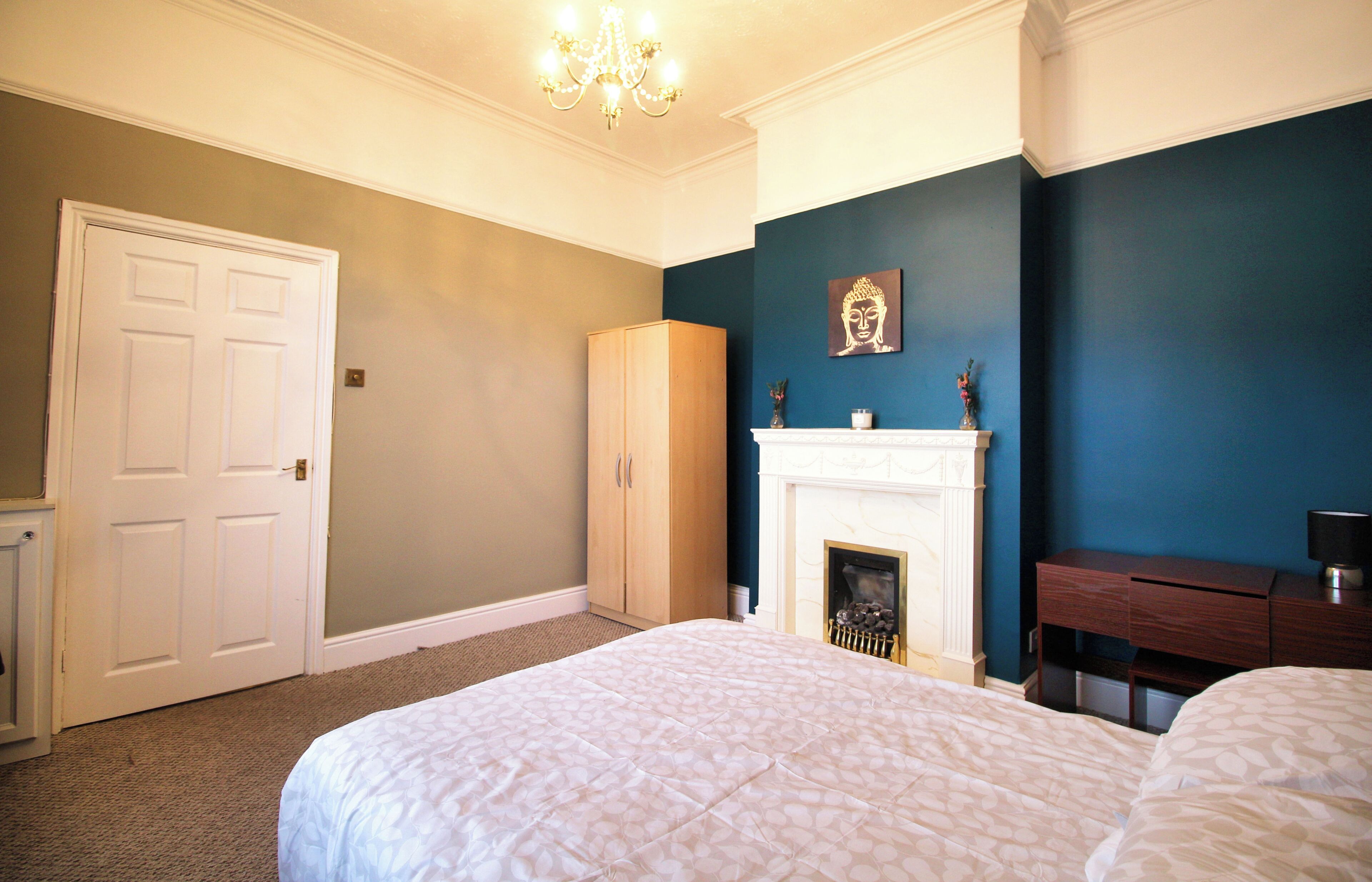 A bedroom with a bed, a wardrobe, a fireplace, and a desk.