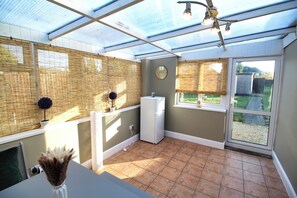 A conservatory with a glass ceiling, a white refrigerator, and a clock on the wall. - Large Bungalow - 3 Beds 2 Baths - Very Large Enclosed Garden - Dogs Stay Free (Birmingham)