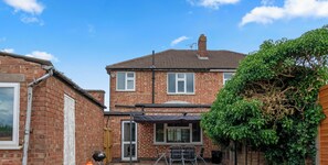 A two-story brick house with a patio area, a barbecue grill, and a bicycle.