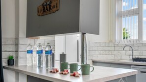 Een keuken met een marmeren aanrecht, waterflessen, groene mokken en een barbord.