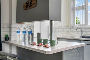 A kitchen with a marble countertop, water bottles, green mugs, and a bar sign.