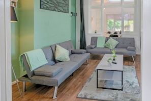 Un salon moderne avec deux canapĂ©s gris, une table basse et une vue sur un coin repas, visible Ă travers une fenĂȘtre.