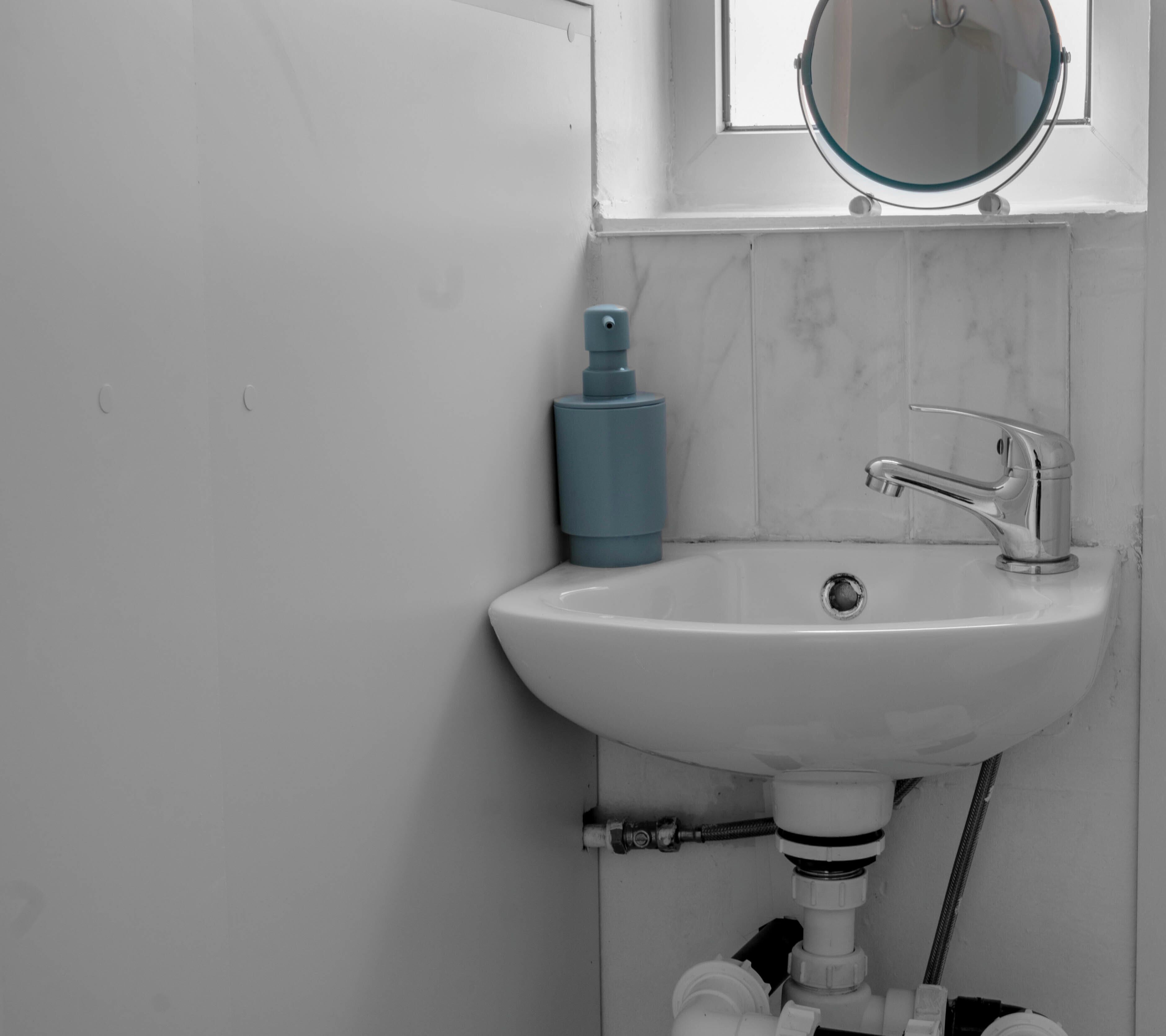 A bathroom with a white sink, a blue soap dispenser, a mirror, and a chrome faucet.
