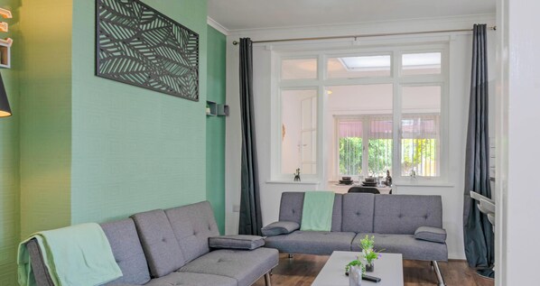 A living room with two grey sofas, a coffee table, and a large window with curtains.