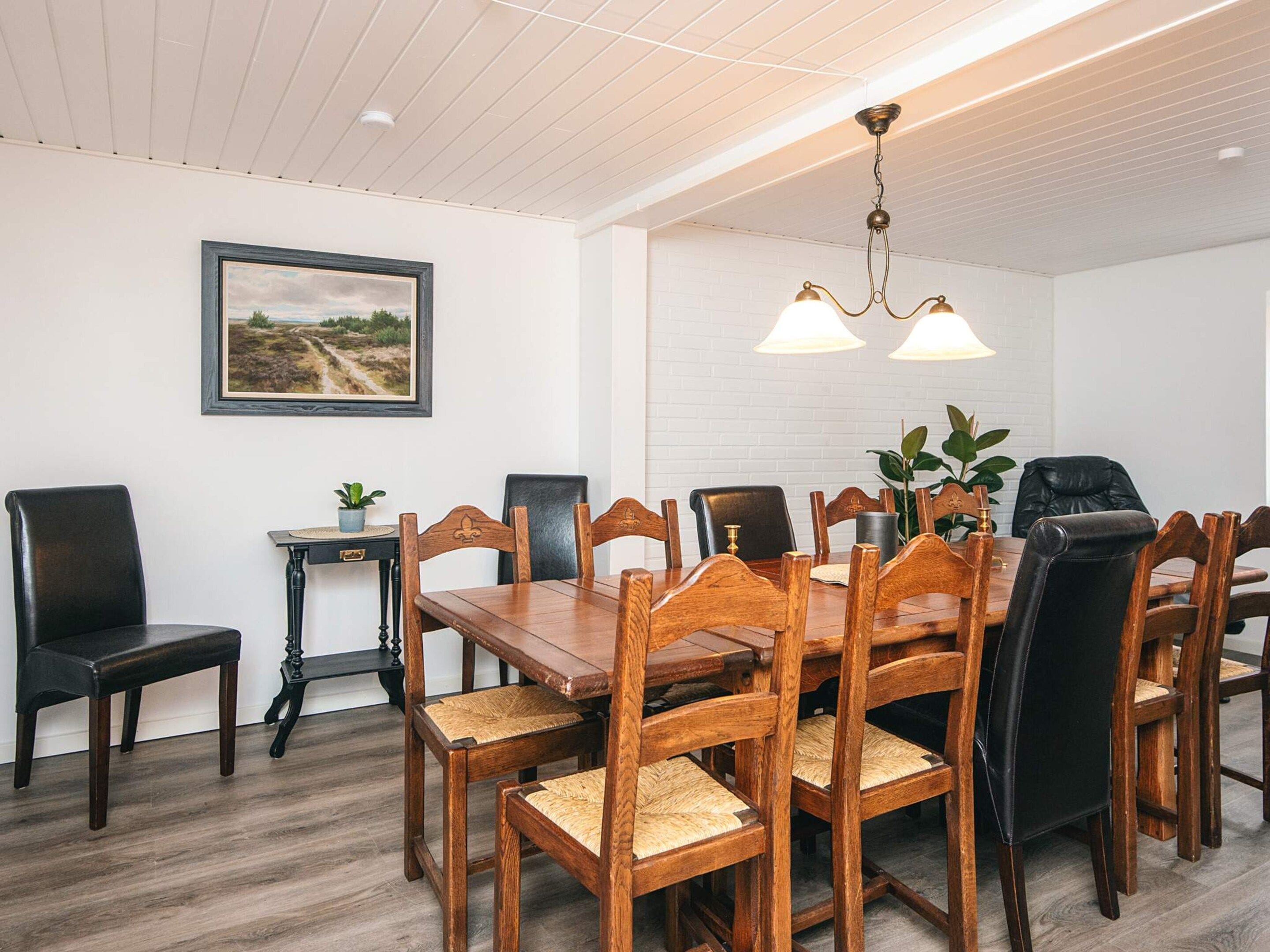 A dining area with a wooden table and chairs, a framed picture on the wall, and a ceiling light fixture.