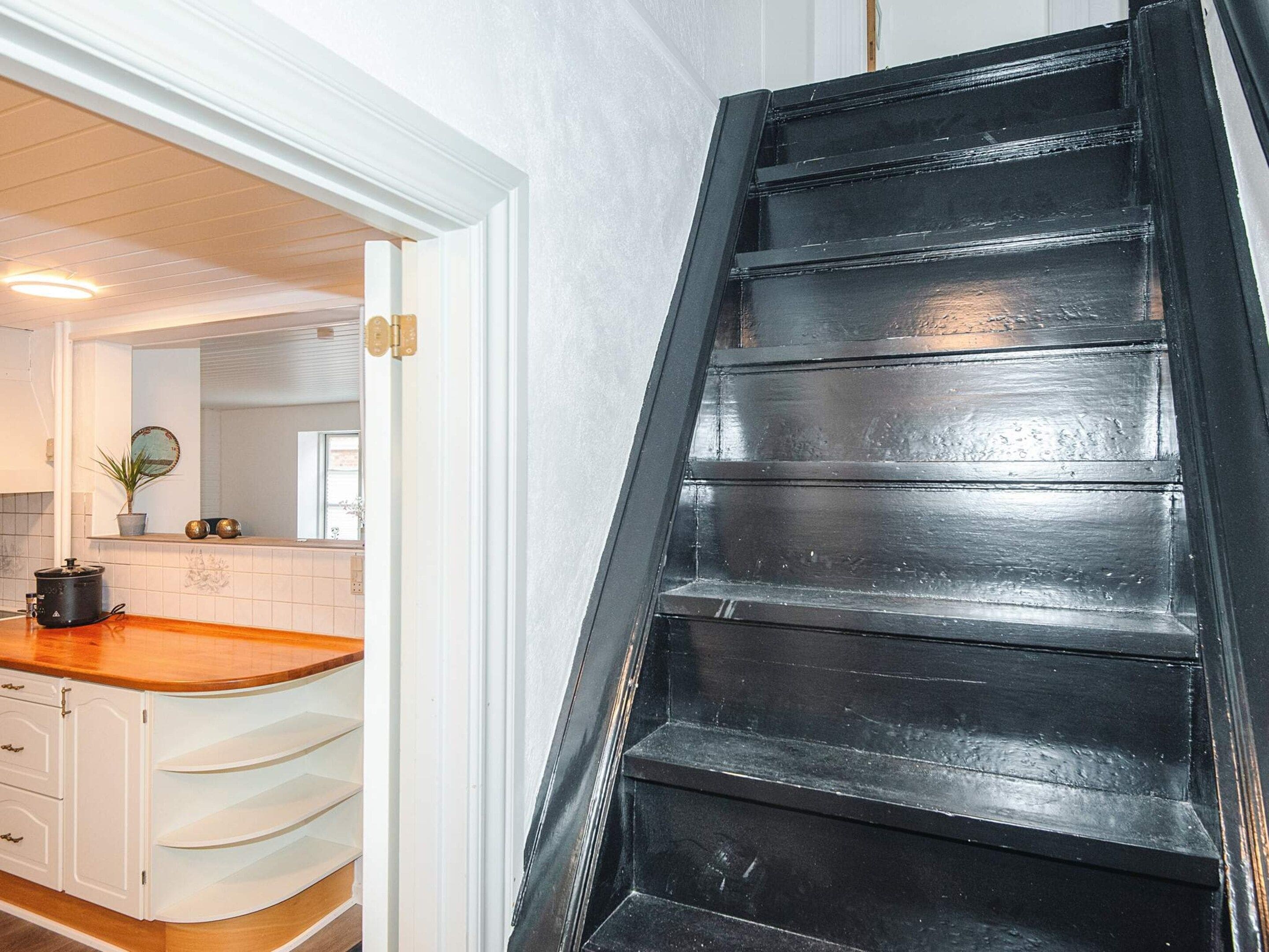 A kitchen with white cabinetry, a wooden countertop, and a black staircase.