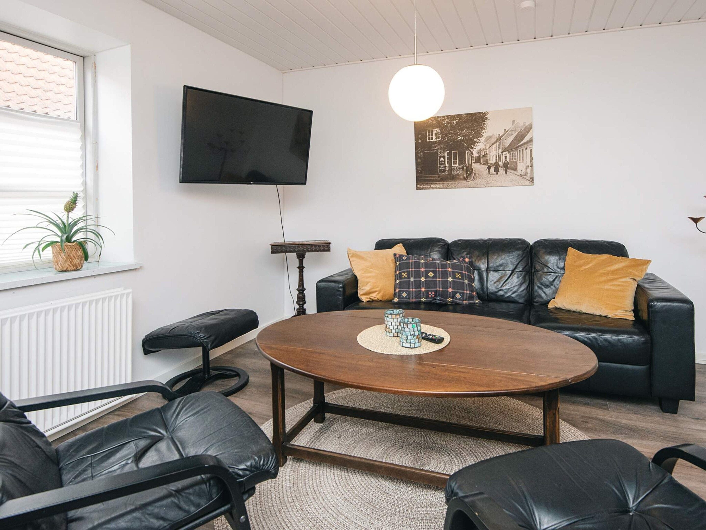 A modern living room with a black leather sofa, a wooden coffee table, and a television mounted on the wall.