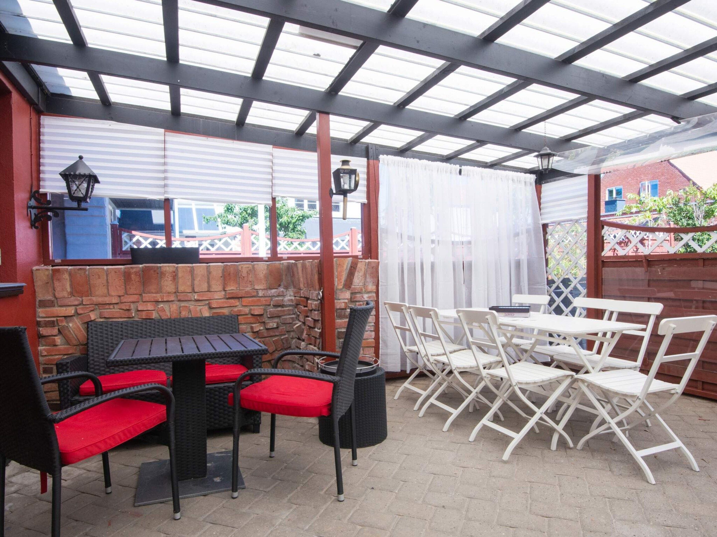 Un patio al aire libre con paredes de ladrillo, una zona cubierta con techo metálico y mobiliario exterior.