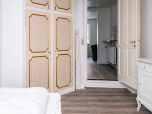 Ein Schlafzimmer mit Bett, einem Schrank mit Spiegel und einem Flur, der zu einer Küchenzeile führt.