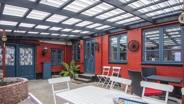 An outdoor patio with white metal tables and chairs, a blue door, and a red wall. - 12 Person Holiday Home in Ringkobing (Ringkobing)