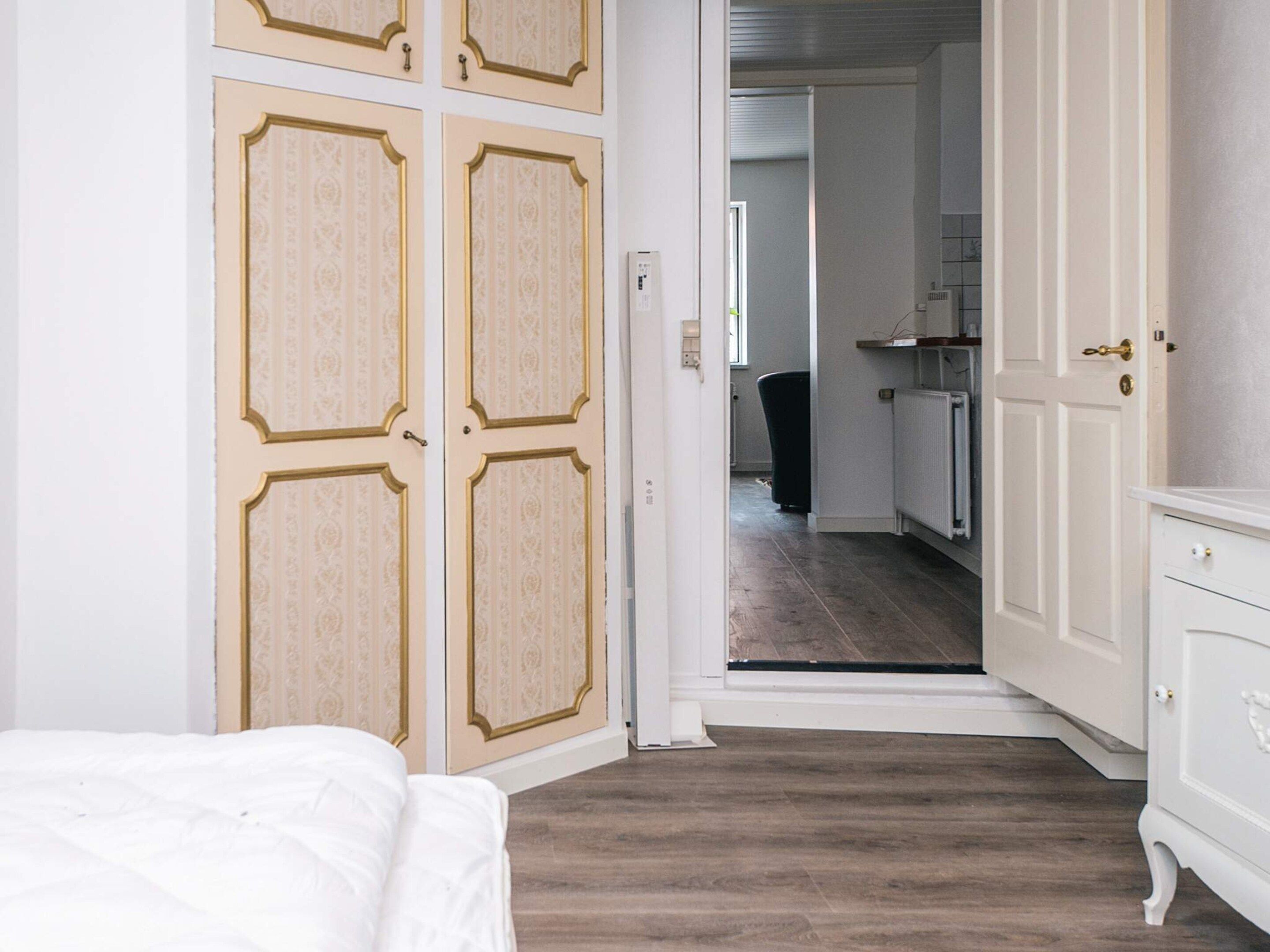 A bedroom with a bed, a wardrobe with a mirror, and a door leading to a hallway.